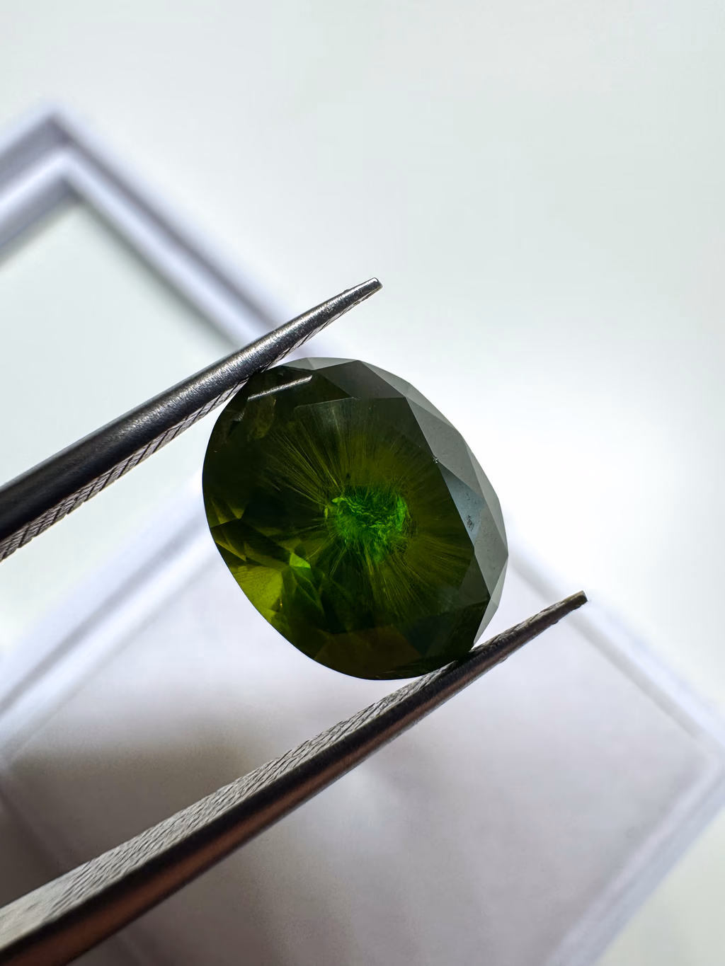 Oval Russian demantoid garnet showing deep bottle-green color and a radiating horsetail inclusion